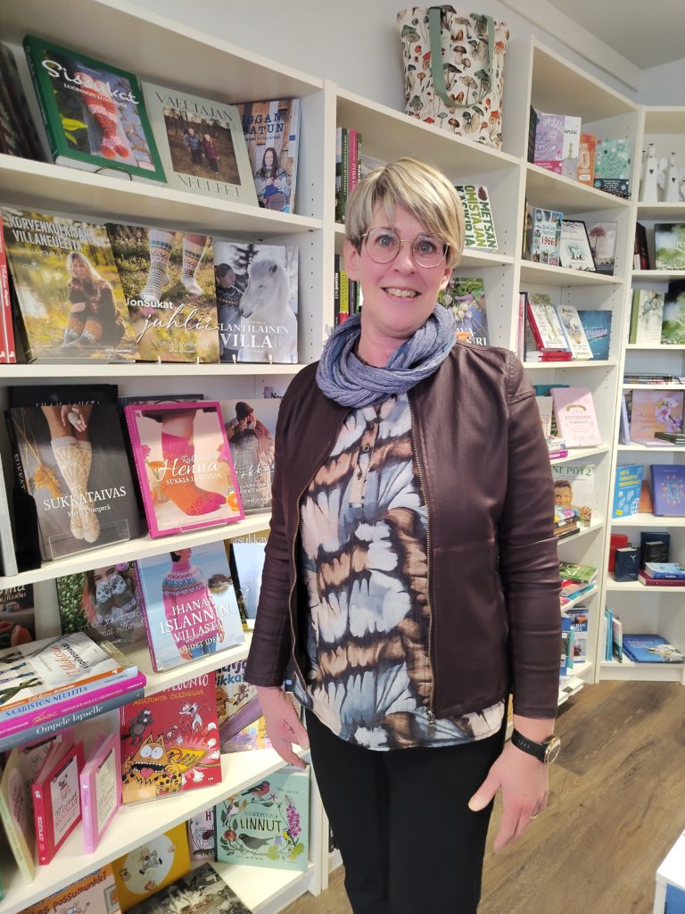 Harjavallan Kirjakaupan Kirjakauppias kirjahyllyn edessä.